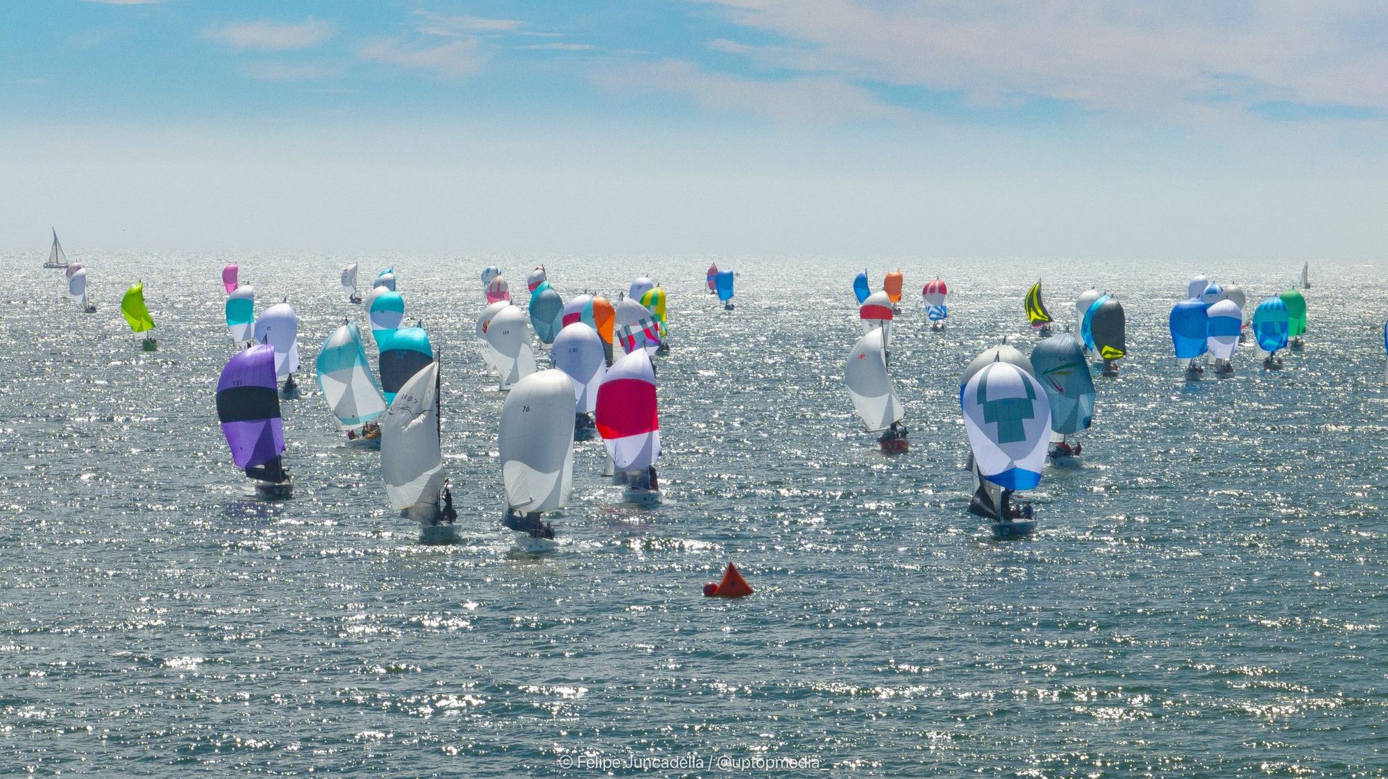 The fleet running downwind past a leeward mark on sparkling water