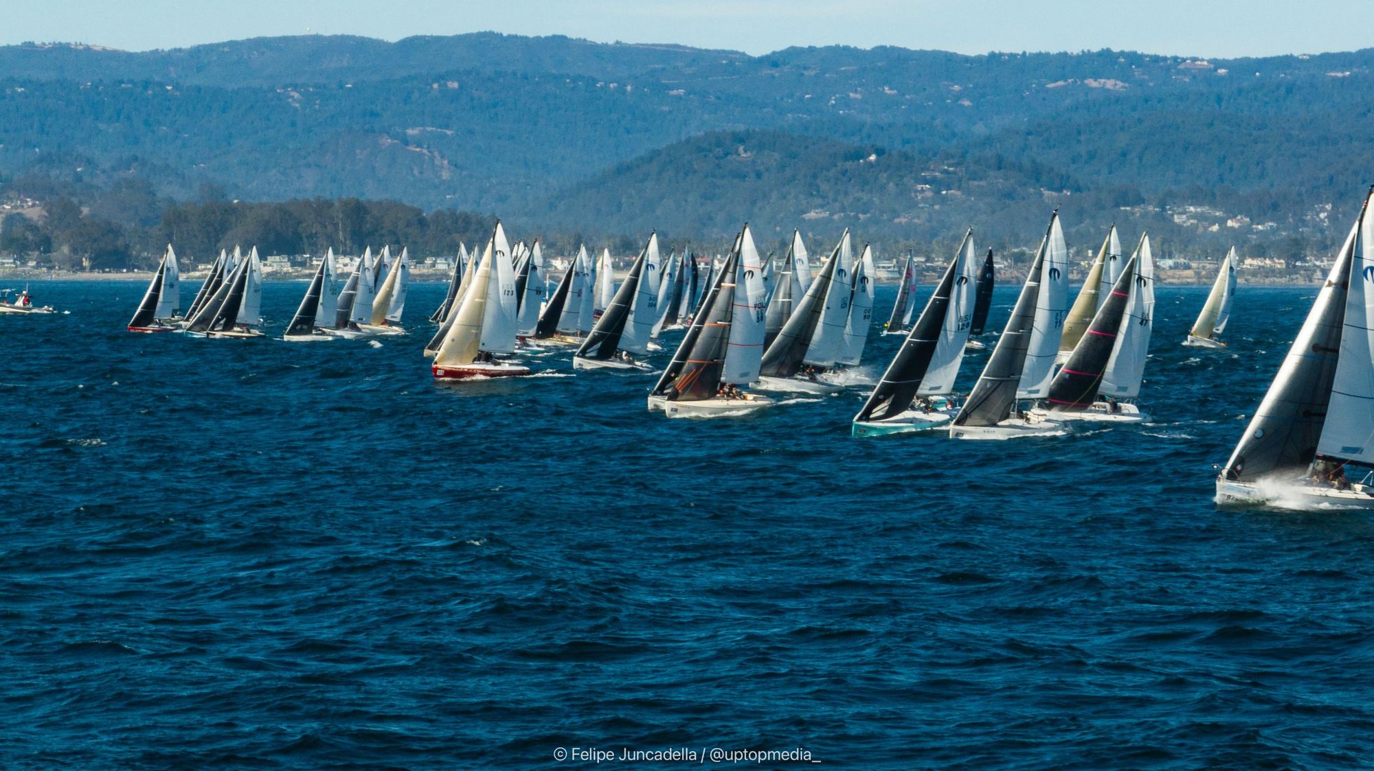 The Moore 24 fleet sailing upwind off a start line with the Santa Cruz hills behind